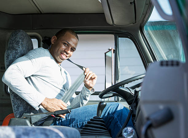 African American man (30s) driving delivery truck, putting on seat belt.